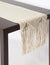 Beige knitted table runner with fringe on a wooden table