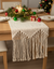 Decorative table runner with fringe on a Christmas-themed table.
