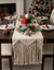 Decorated Christmas table with a macrame runner, candles, and a tree in the background.
