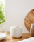 White marble container with gold base on a wooden surface with a jar of oats and plant in the background.