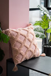 Pink textured pillow on a black surface with plants in the background