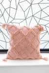 Pink textured pillow with tassels on a white surface with a geometric black and white patterned wall in the background.