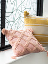 Pink textured pillow with tassels on a windowsill with a yellow and white striped pillow in the background.