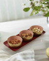 Three bowls of nuts on a tray with a pear and flowers in the background