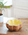 Wooden bowl with yellow interior on a wooden surface, blurred plant in the background