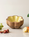 Wooden fruit bowl with a yellow interior on a light surface with fruits around