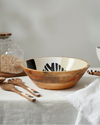 Wooden bowl with black design on a table with jars and utensils.