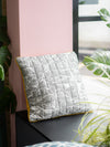 Gray pillow with leaf pattern on a surface near a window with pink wall and green plants.