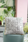 Quilted pillow with floral pattern on a teal stool with plants in the background