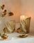 Gold leaf candle holders with a lit candle on a soft surface with flowers.