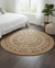 Round woven rug in a bedroom with a bed, plant, and ottoman.