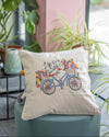 Decorative pillow with bicycle and floral design on a chair with plants in the background