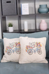 Two decorative pillows with bicycle and floral design on a blue couch.