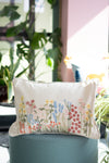 Decorative pillow with floral embroidery on a teal chair in an outdoor setting with plants.