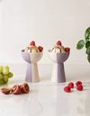 Two ceramic dessert bowls with ice cream and fruit on a white surface.