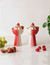 Two red and white ceramic bowls with ice cream and berries on a light surface.