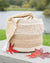 Woven basket with a blanket draped over it, surrounded by autumn leaves by a body of water.