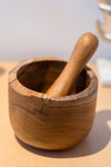 A handcrafted teak wood mortar and pestle set placed on a table, showcasing the natural wood grain and the craftsmanship.