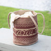 Woven basket with a pattern on a wooden surface with grass in the background