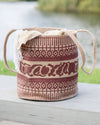 Woven basket with decorative patterns on a wooden surface by a body of water.
