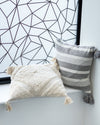 Two pillows, one white and one gray with stripes, against a geometric-patterned wall.