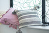 Decorative pillows with tassels on a surface with a geometric window pattern in the background.