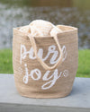 Jute bag with 'pure joy' text on a wooden surface with a blurred natural background