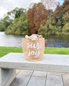 Woven basket with 'pure joy' text on a bench by a lake