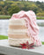 Woven basket with a pink blanket draped over it by a lake