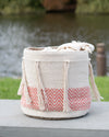 Textile basket with tassels and a pink zigzag pattern on a wooden surface with a blurred natural background.