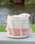 Textile basket with tassels and a pink zigzag pattern on a wooden surface with a blurred natural background.