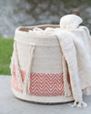 Textile basket with a white blanket draped over it, set against a blurred natural background.