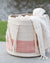 Textile basket with a white blanket draped over it, set against a blurred natural background.