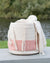 Woven bag with pink pattern and white tassels on a wooden surface with a blurred natural background