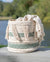 Macrame basket with tassels and geometric patterns on a wooden surface with a blurred natural background