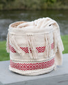Woven basket with red patterns and white tassels on a wooden surface with a natural background