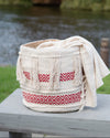 Decorative woven basket with red patterns on a wooden surface near a body of water.