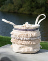 Decorative woven basket with tassels on a wooden surface outdoors.