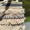 Close-up of a woven basket with fringes and a black and white striped band on a blurred natural background.