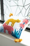 Colorful embroidered pillow with animals and flowers on a window sill.