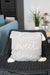 Gray pillow with 'home sweet home' text on a wicker chair in a blurred indoor setting