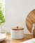White container with wooden lid, glass jar with wooden lid, and cutting board on a wooden surface.