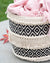 Decorative woven basket with black and white geometric pattern and pink fabric on a light surface.