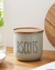 Biscuits container with wooden lid on a kitchen counter with a plant and jar in the background