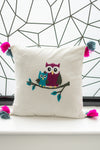 Decorative pillow with embroidered owls on a branch against a geometric wall.