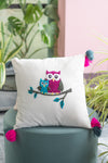 Decorative pillow with owl design on a green chair, surrounded by plants.