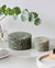 Two green marble boxes on a white surface with a plant and towel in the background.