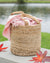 Woven basket with a pink blanket on a wooden surface near a body of water
