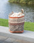 Woven basket with patterned design on a wooden bench by a body of water.