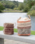 Two woven baskets with patterned designs on a wooden bench by a lake.